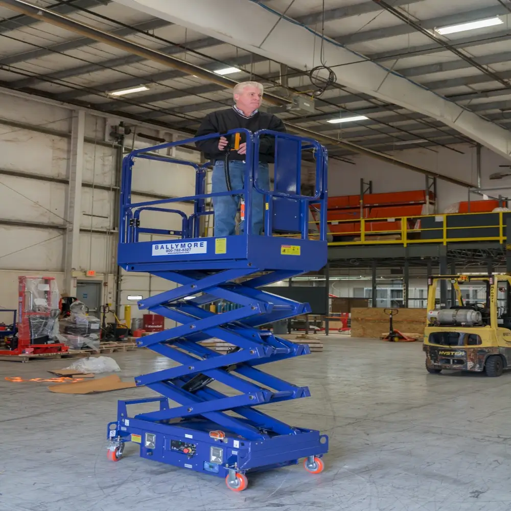 A worker stands on a raised blue scissor lift inside a warehouse to safely perform tasks at height