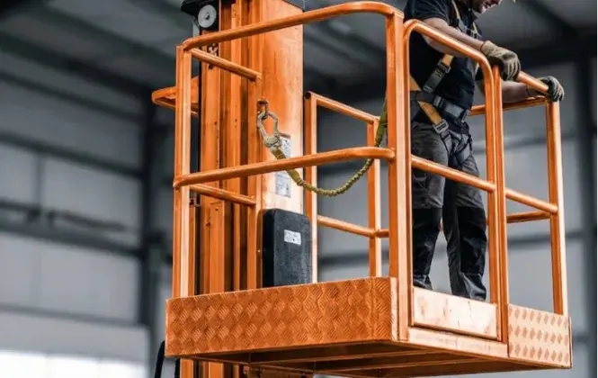 Worker in harness on a bright orange vertical mast lift platform.
