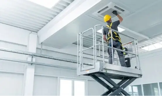 Worker in safety harness using scissor lift for ceiling maintenance.